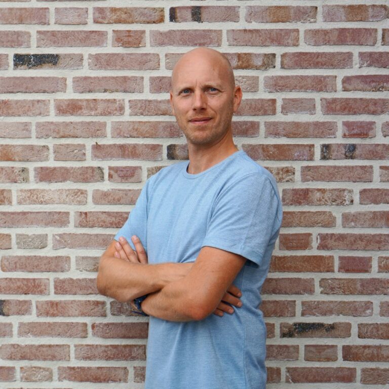 Yuri Dingemans staat met gevouwen armen voor een bakstenen muur.