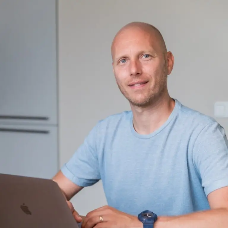 Yuri Dingemans in lichtblauw t-shirt die achter een laptop zit aan tafel.
