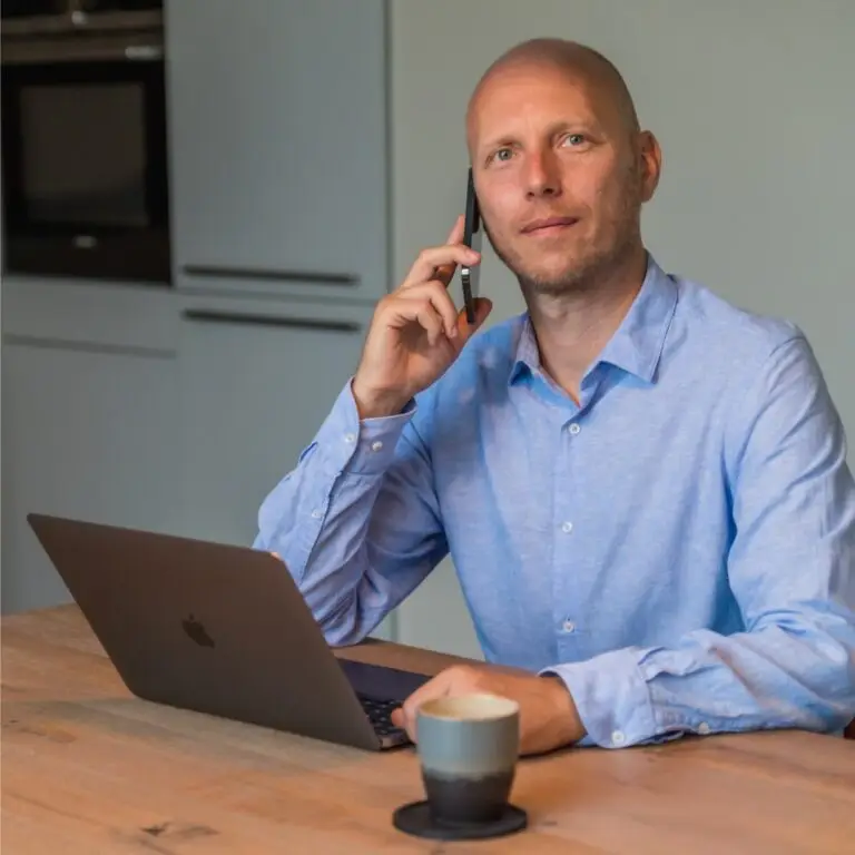 Yuri Dingemans belt met een mobiele telefoon achter een laptop aan een keukentafel.
