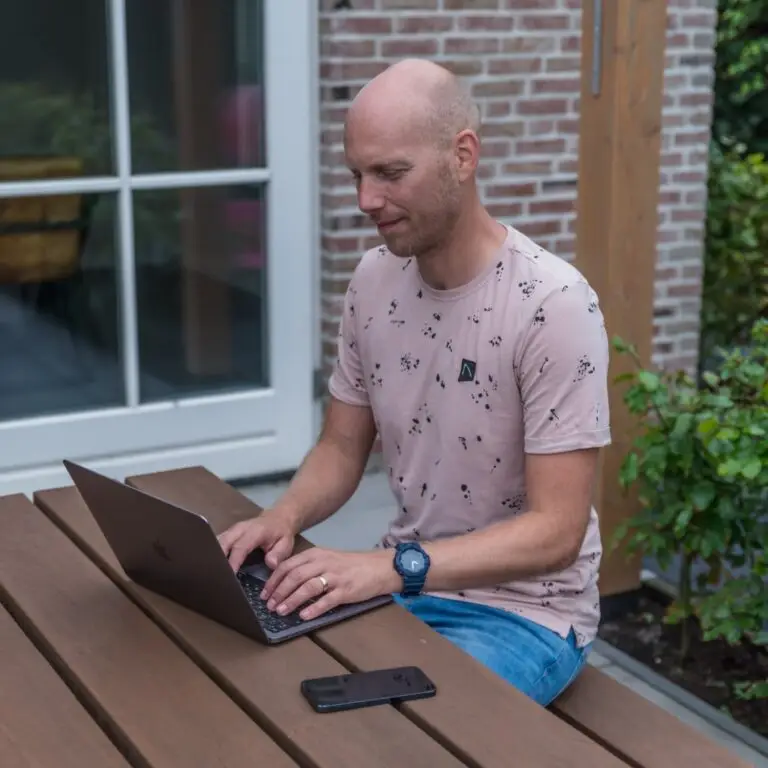 Yuri Dingemans die achter een laptop zit aan een picknicktafel in de tuin.